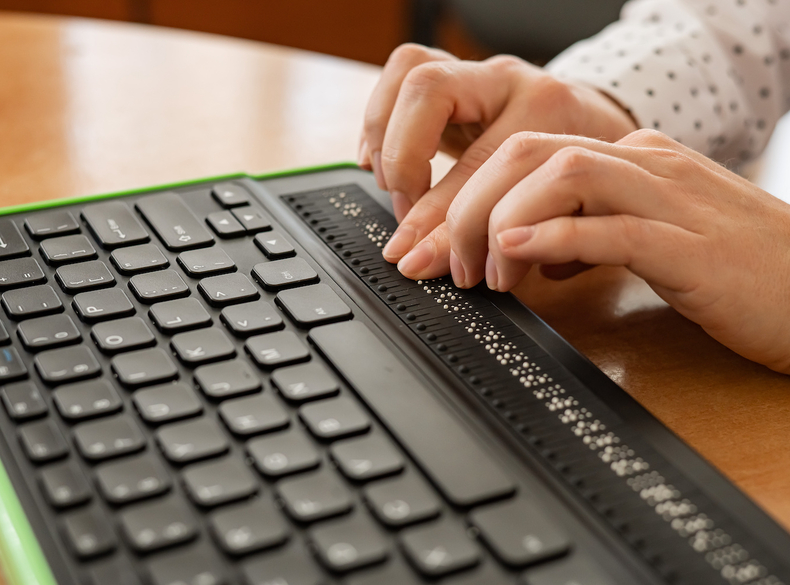 Zwei Finger berühren eine Tastatur für Blinde und Sehbinderte